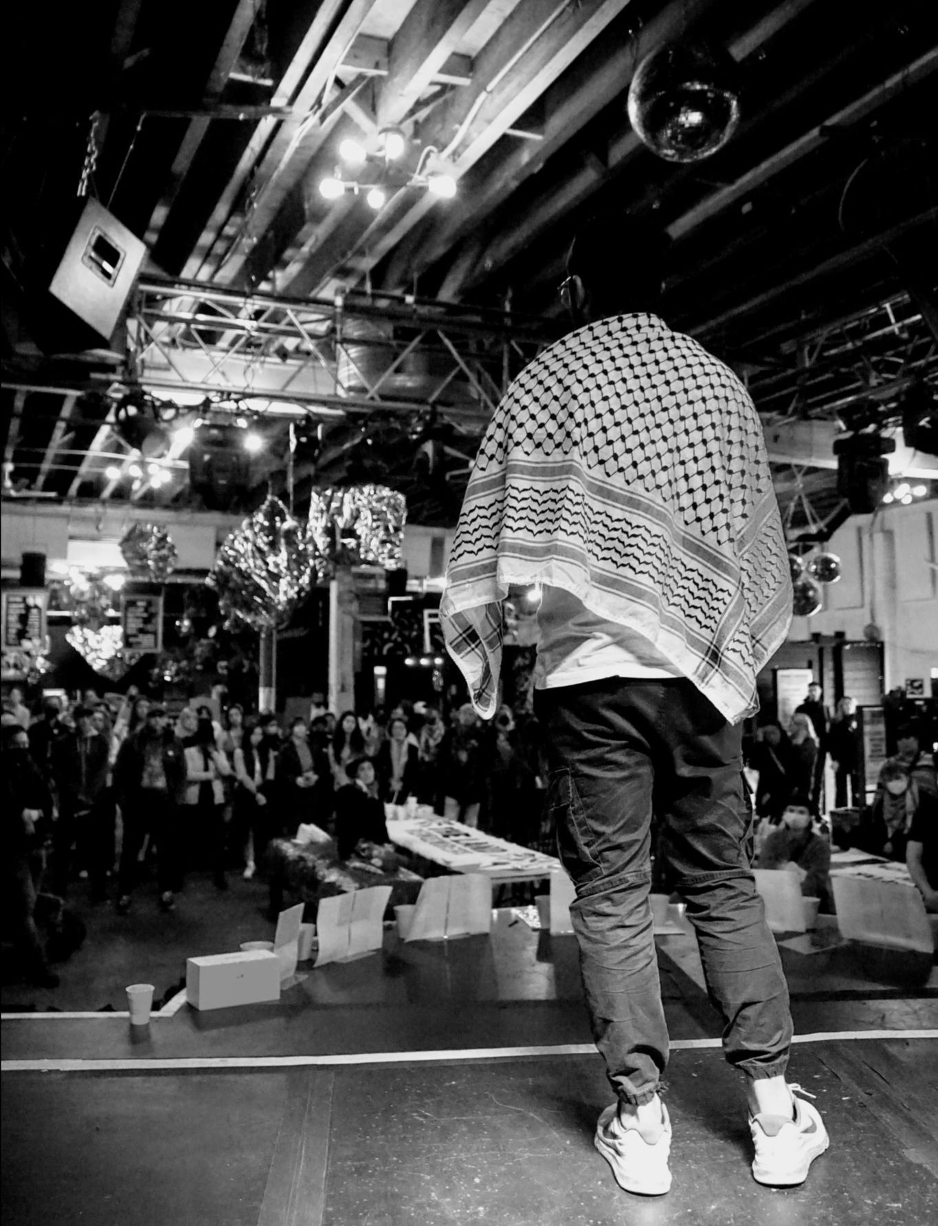 A person standing on a stage in front of a crowd wearing a keffiyeh