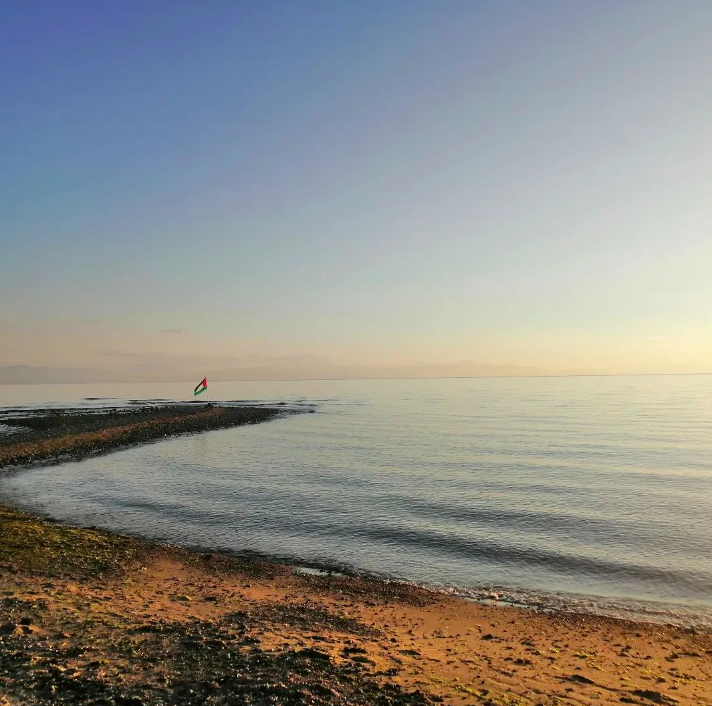a view of the beach and the ocean at sunset with a Palestinian flag waving in the distance