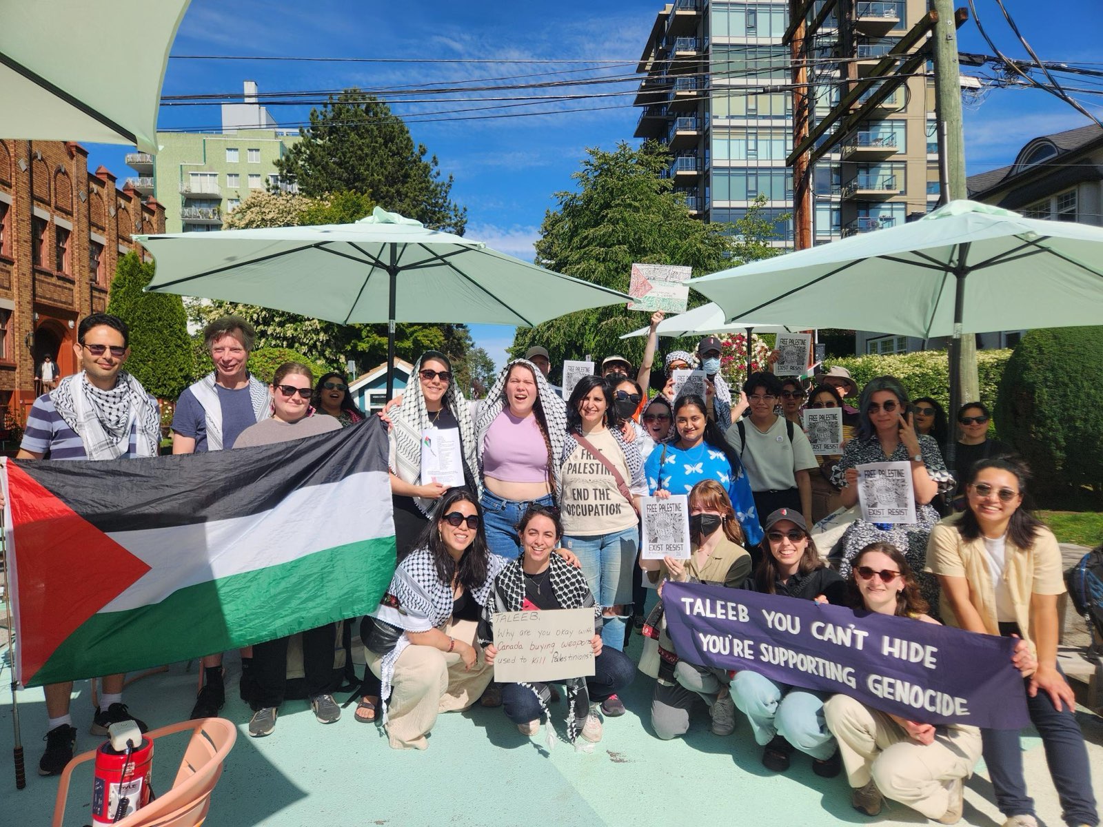 a group of people holding a Palestinian flag, banners and signs